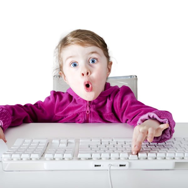 Kind drückt au eine Tastatur und schaut überrascht