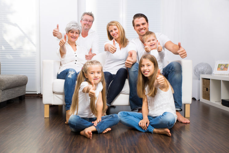 Eine Familie sitzt gemeinsam auf einem Sofa und zeigt Daumen hoch