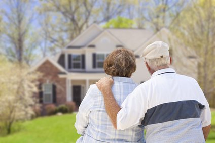 Ein älteres Pärchen steht Arm in Arm vor einem Haus