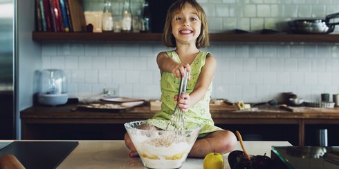 Ein Mädchen sitzt glücklich auf der Küche und rührt Teig um