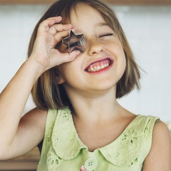 ein Mädchen hält sich lächelnd einen Keksausstecher vor das Gesicht