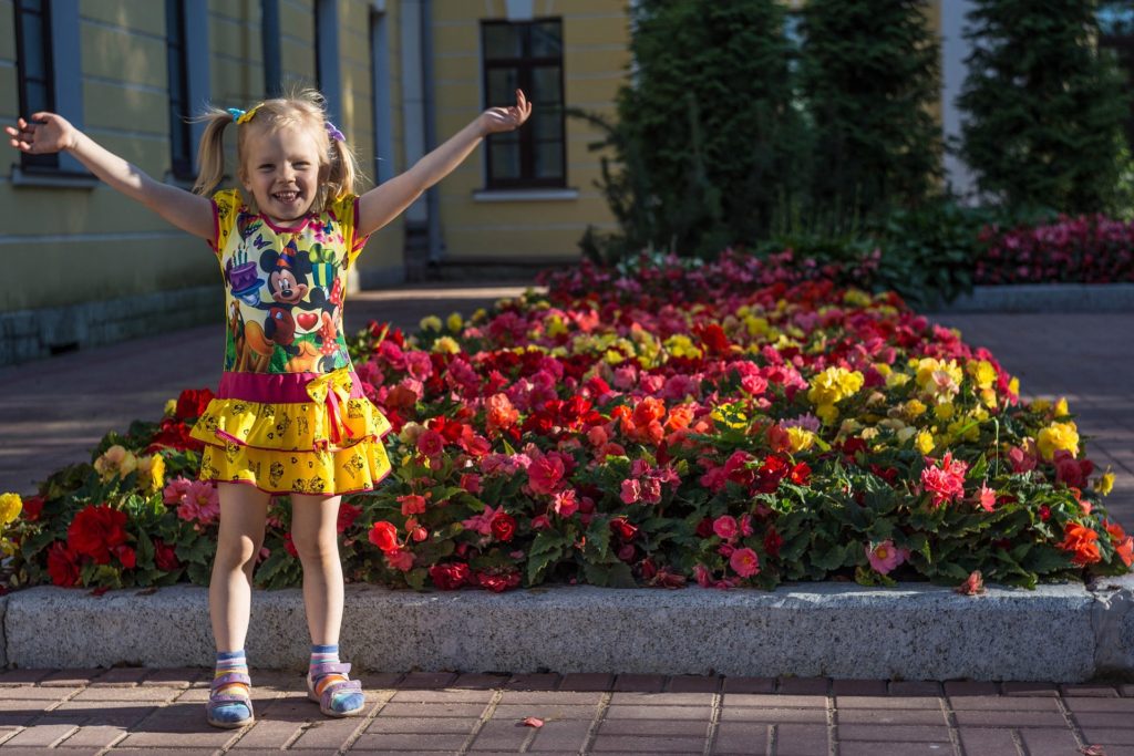 kleines Mädchen steht freudig vor einem Blumenbeet