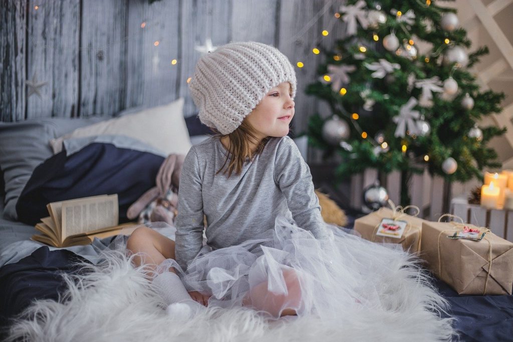 kleines Mädchen sitzt neben Geschenken und trägt eine Wollmütze